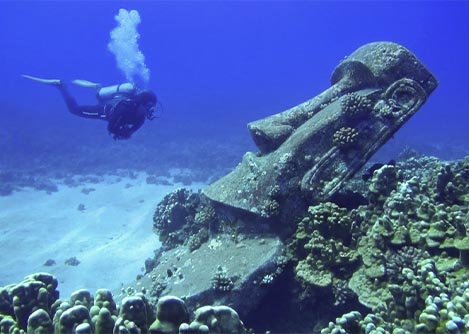 A scuba diver swimming near an underwater moai, the monolithic figures found on Easter Island.