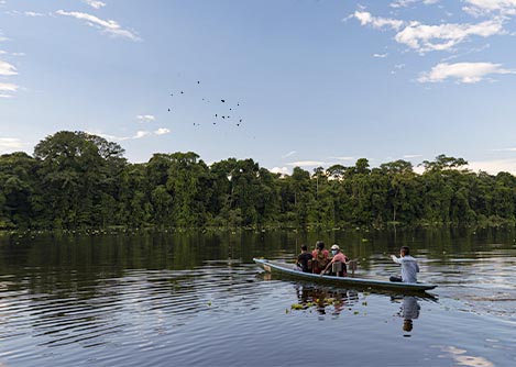 A few visitors on a canoe navigating a river surrounded by forest in the Ecuadorian Amazon.