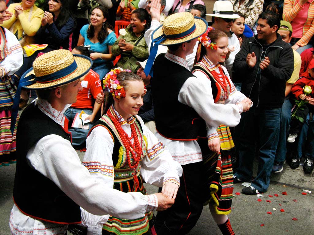 Several pairs of dancers hold hands and dance in the Ambato carnival parade.