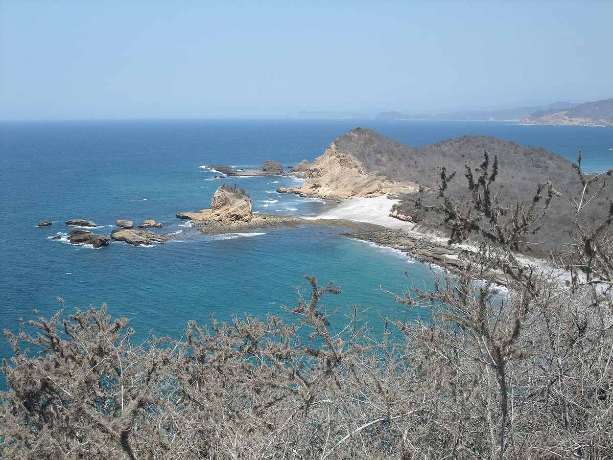 Brown vegetation and a small rocky peninsula in the blue waters of Machalilla National Park.