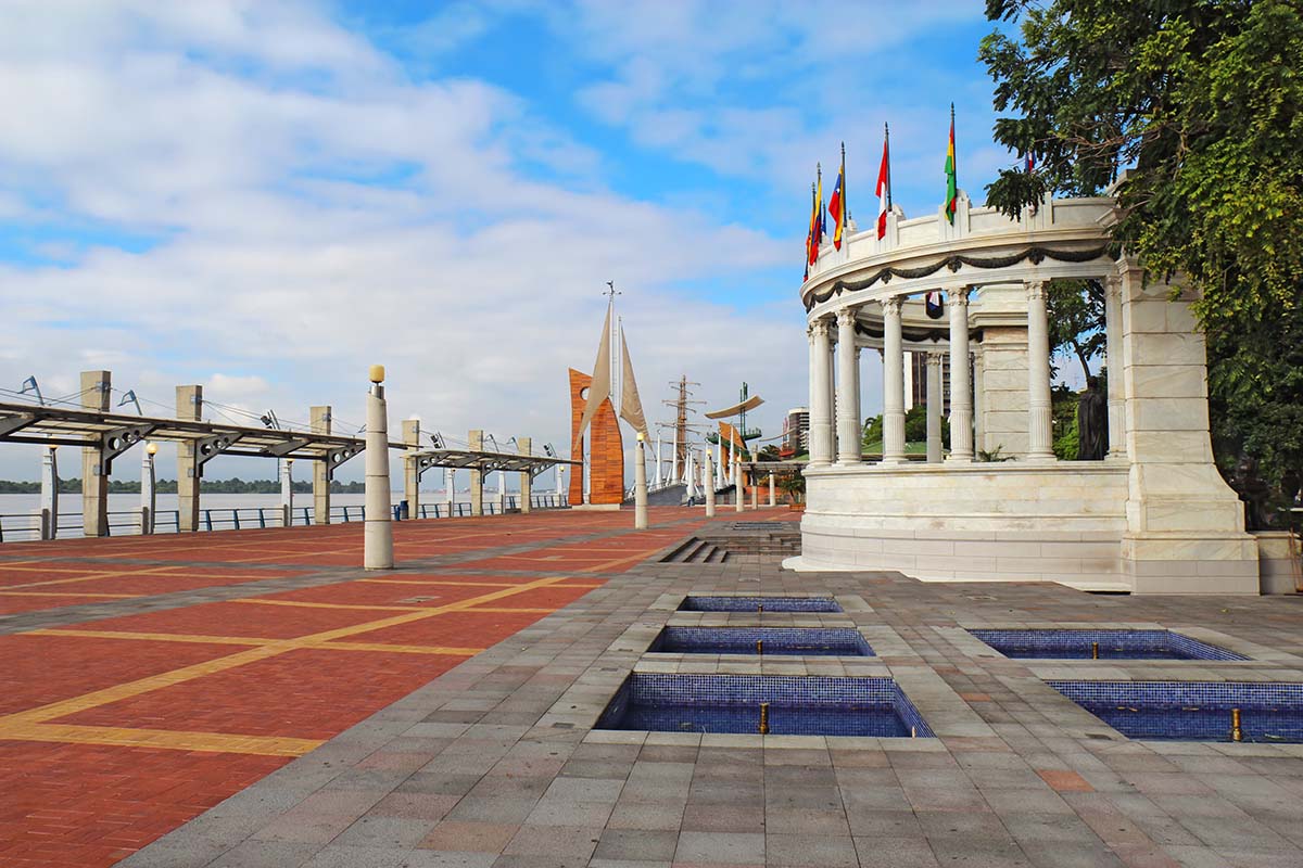 A wide, brown sidewalk along a river with art installations and trees in Guayaquil.