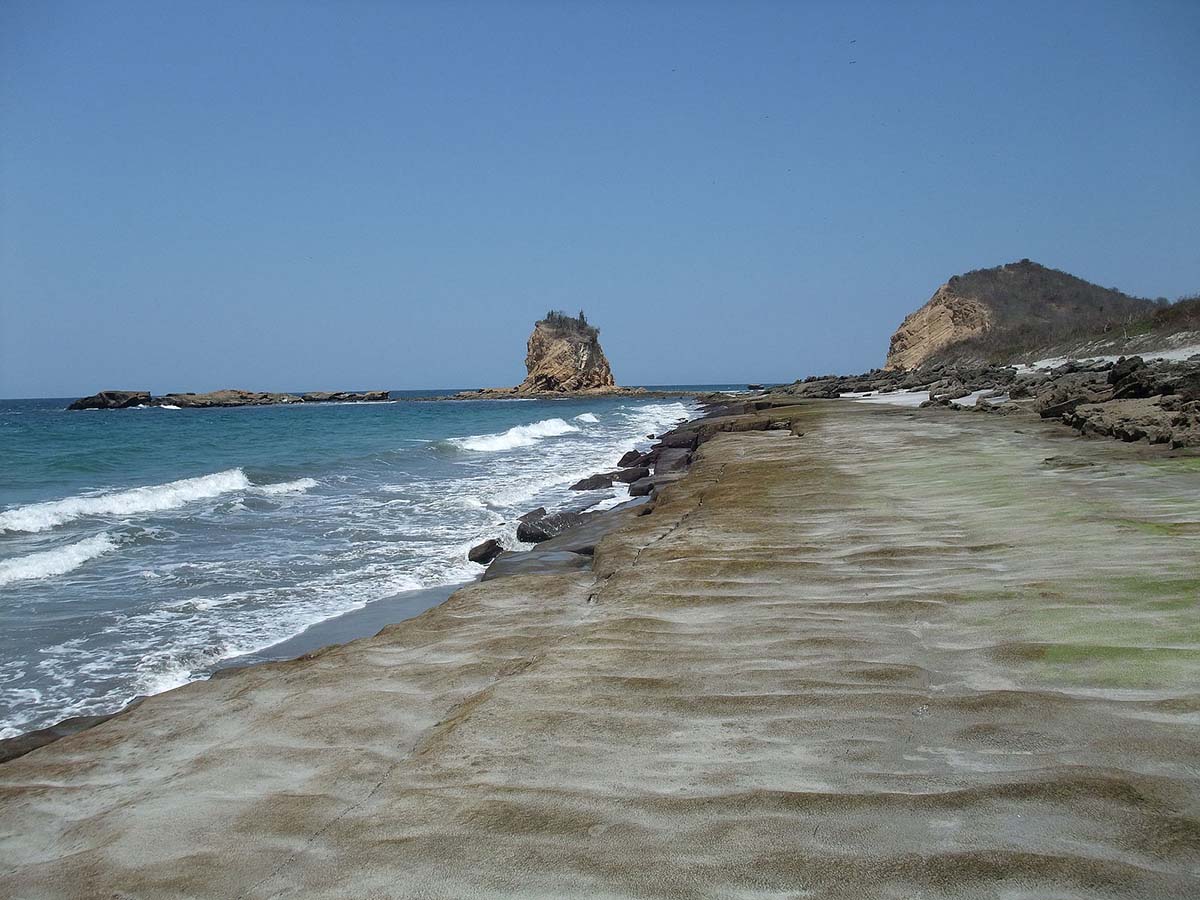 A long sandy beach with rock formations on the land and in the water at Machalilla National Park.