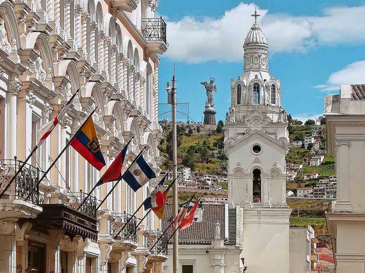 White stone building with flags sits next to a path leading to the Quito Metropolitan Cathedral.