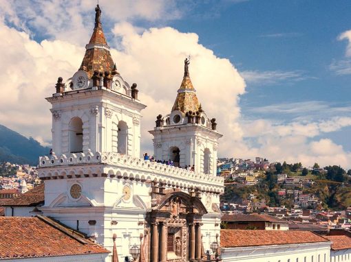 A white church, the San Francisco Monastery in Quito, with brown roof and accents and two spires.