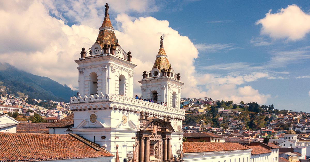 A white church, the San Francisco Monastery in Quito, with brown roof and accents and two spires.