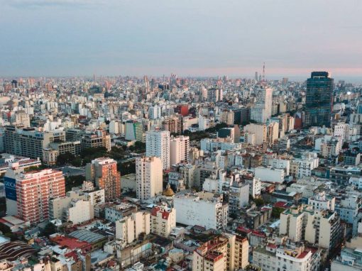 An aerial view of the sprawling Buenos Aires cityscape in front of a blue and pink sky.