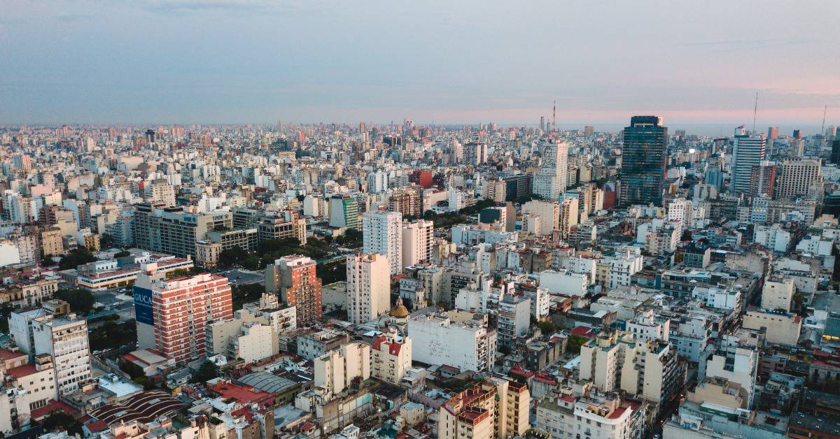 An aerial view of the sprawling Buenos Aires cityscape in front of a blue and pink sky.