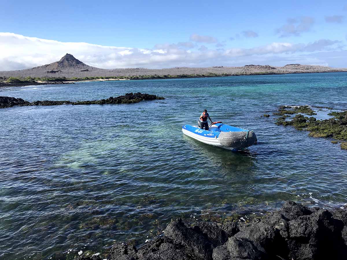 Black rocky shores with a dinghy approaching. Tall, black peak in the background.