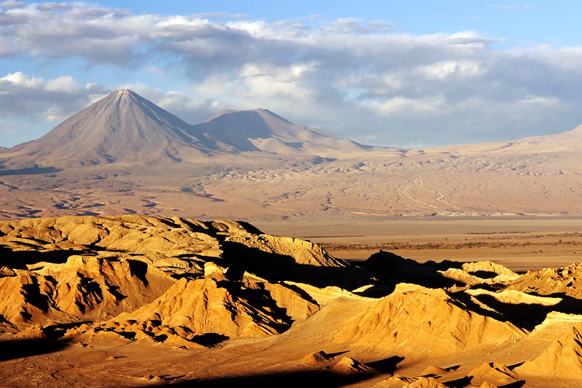 Orange sandy terrain with a mountain stretching above the horizon in the Atacama Desert.