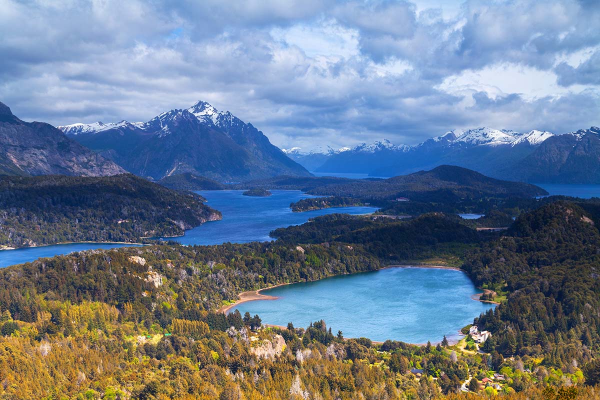 Several blue lakes surrounded by lush forest and tall mountains in the distance.