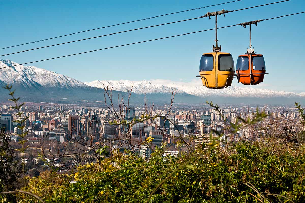 Two cable cars cross paths with Santiago, Chile and the surrounding mountain landscape behind.