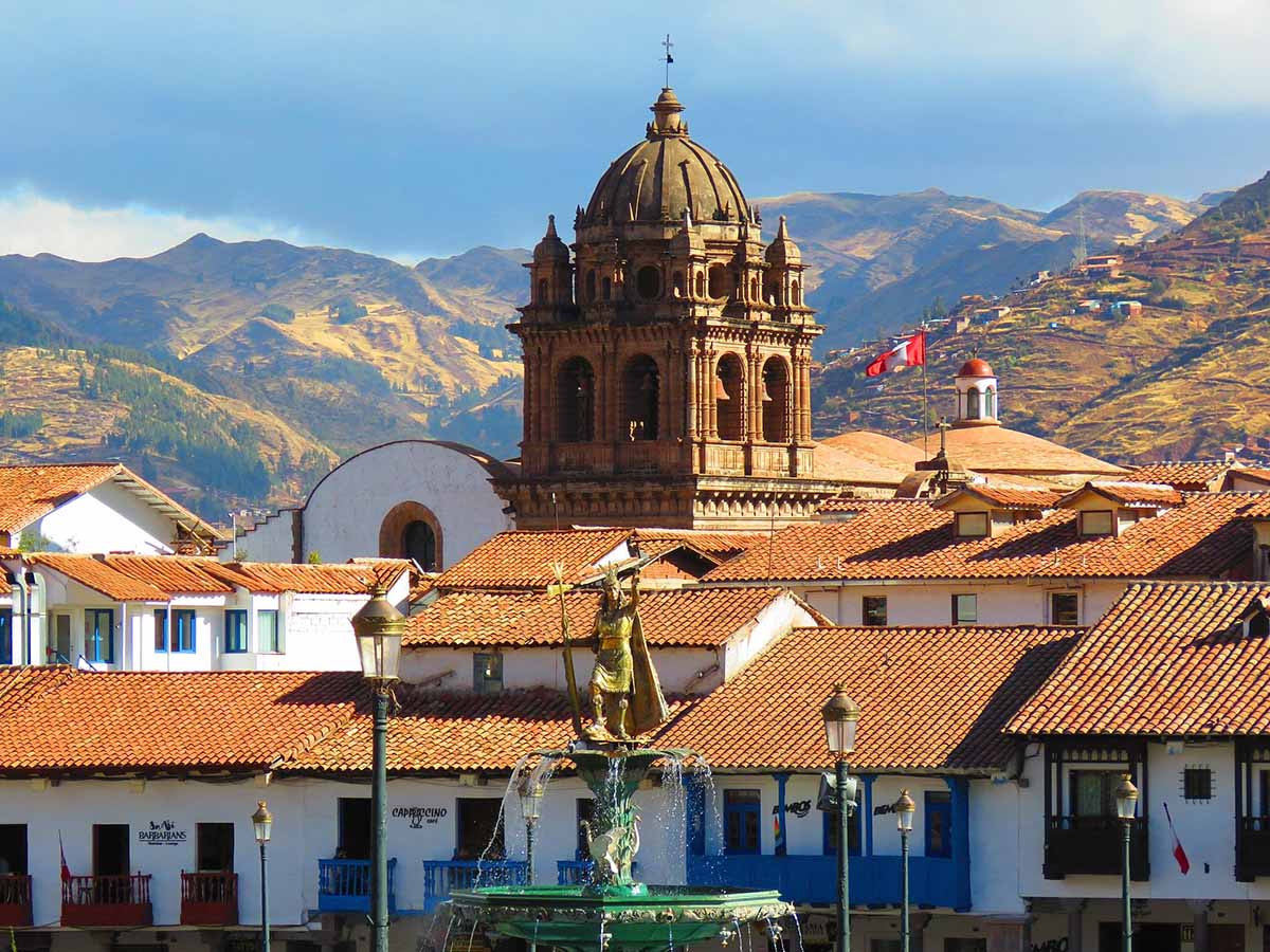Coricancha's dome pierces the sky with red-roofed colonial buildings surround it.