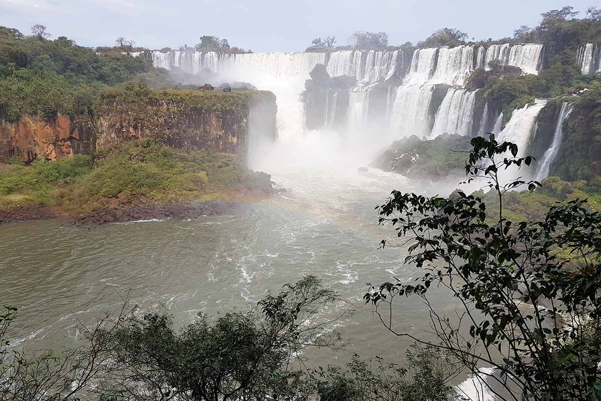 Trees and a rainbow in view with endless waterfalls stretching in the background.