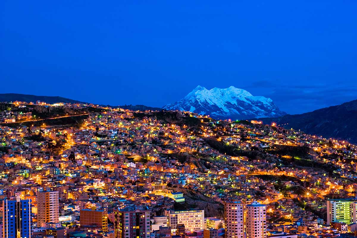 La Paz at night, with the city full of light and a snow capped mountain behind.