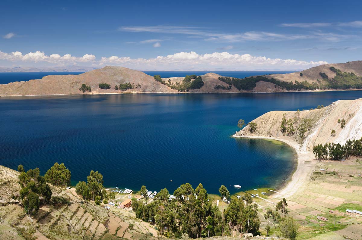 Tan and green landscape leads to dark blue water with a small piece of land above.