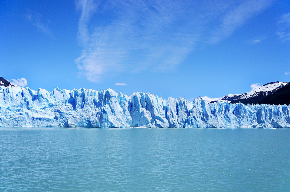 Shades of light blue distinguish the bright sky, thick glacier, and icy lake below.