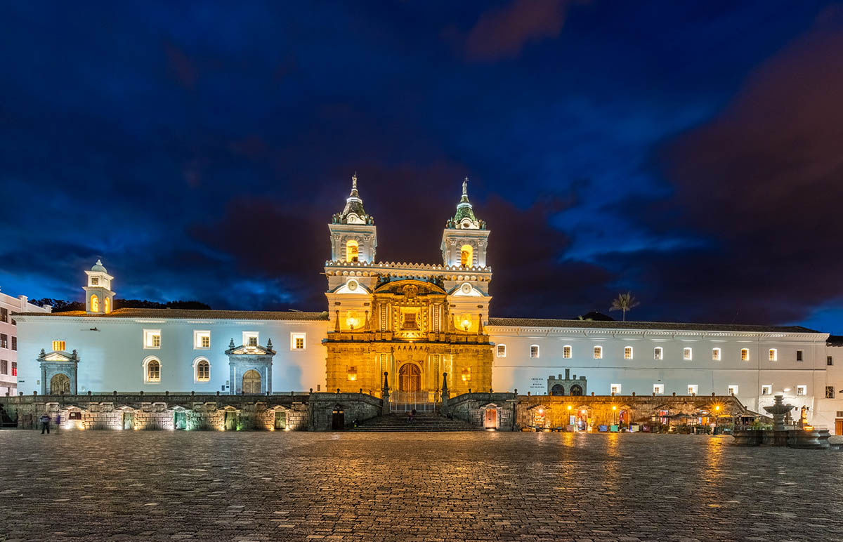 A long, lit up building sits on the other side of a stone plaza in Quito.