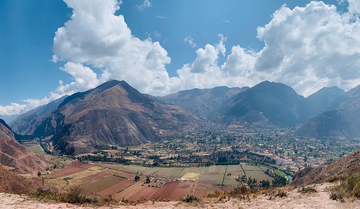Panoramic view of the Sacred Valley surrounded by tall Andes Mountains and cloudy skies.