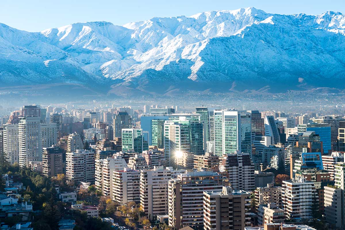 Tall buildings packed into Santiago with massive mountains behind. 
