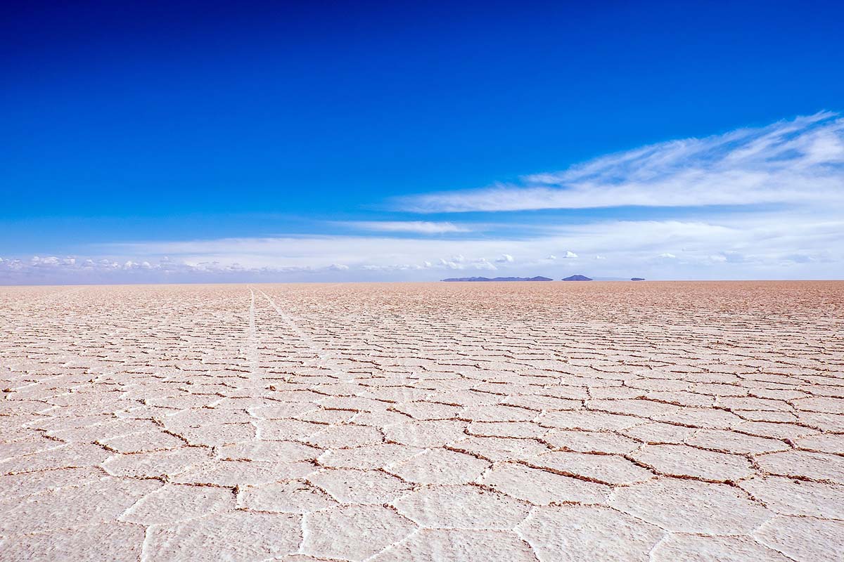 Light pink salt flats stretch to the horizon under a bright blue sky.