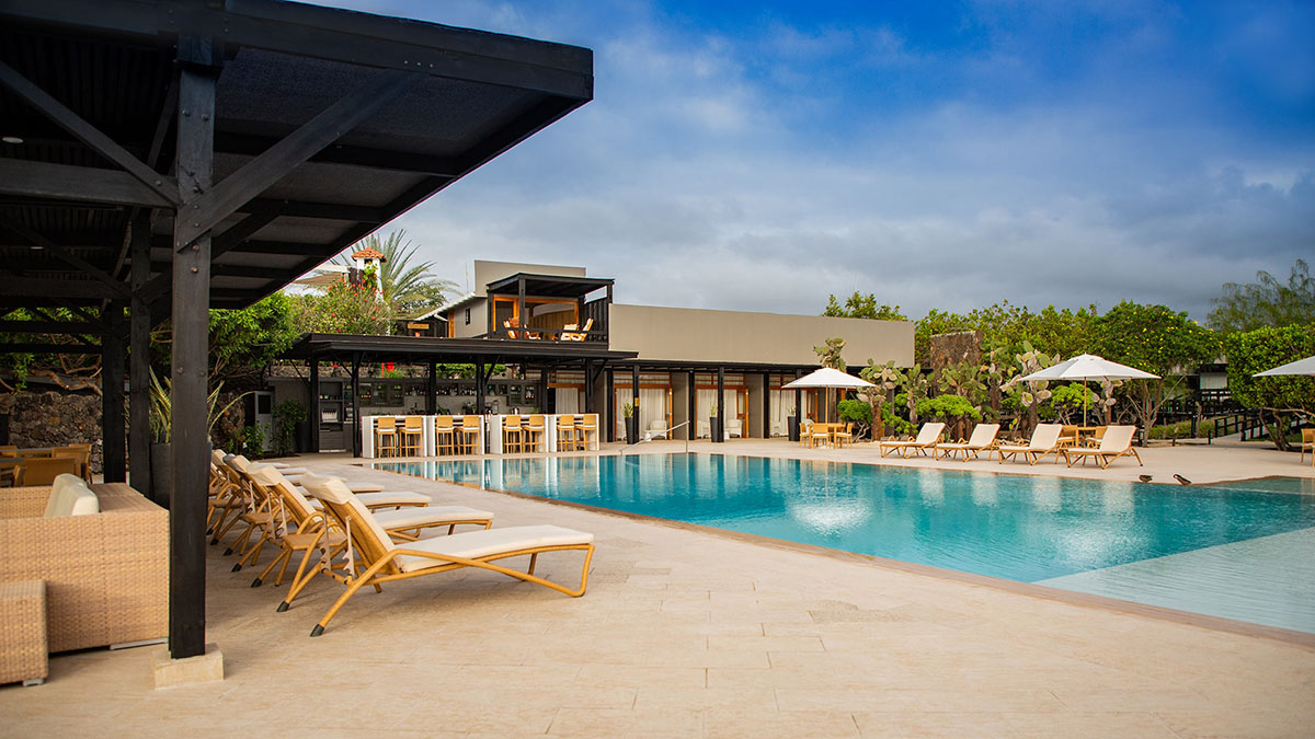 A large pool surrounded by lounge chairs and the main building of Finch Bay Hotel.