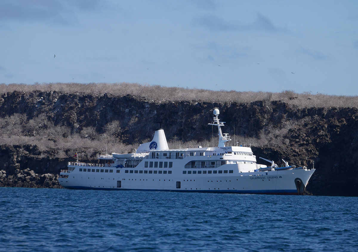 A Galapagos cruise ship floating in the ocean with a rocky island behind.