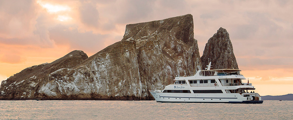The Sea Star cruise ship sailing in front of Kicker Rock, a jagged rock formation, at sunset.