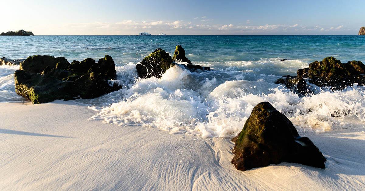 Ocean waves crash onto white sand on one of the galapagos island beaches on Espanola Island.