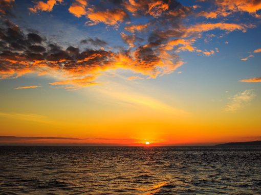 The sun sets over the ocean in the Galapagos, filling the blue sky with orange and red clouds.