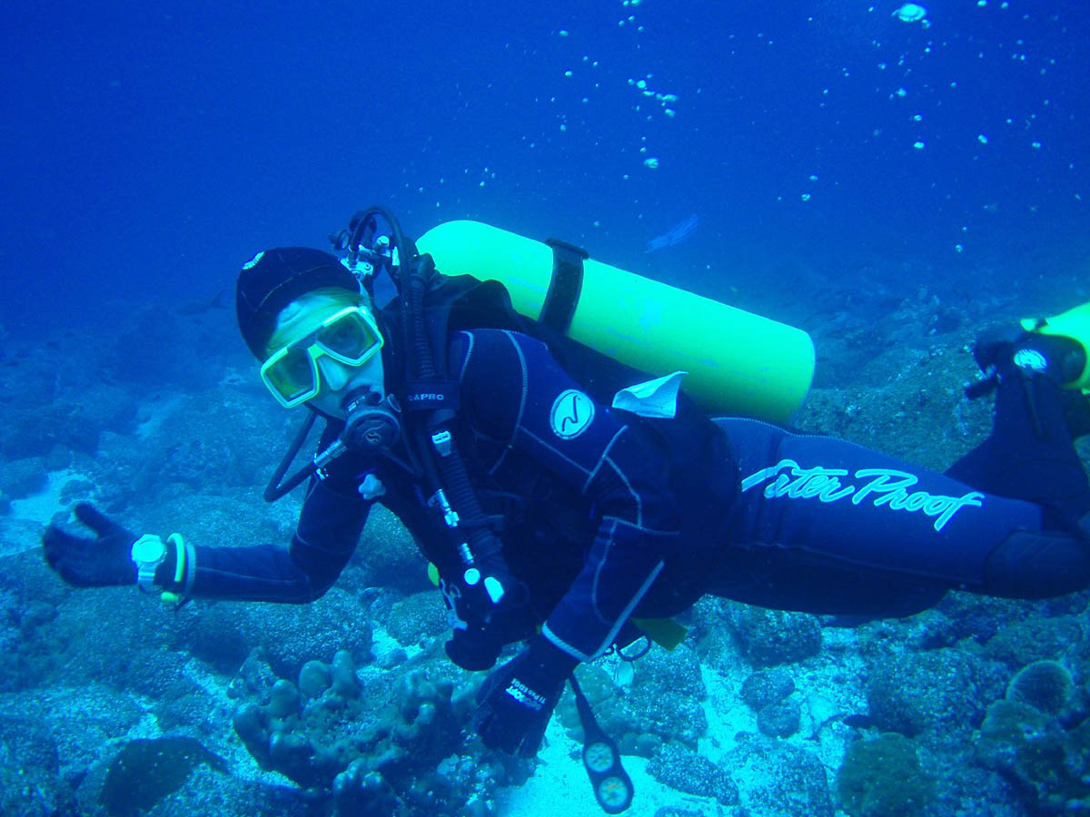 A person with a yellow dive mask and oxygen tank diving near the ocean floor in the Galapagos.