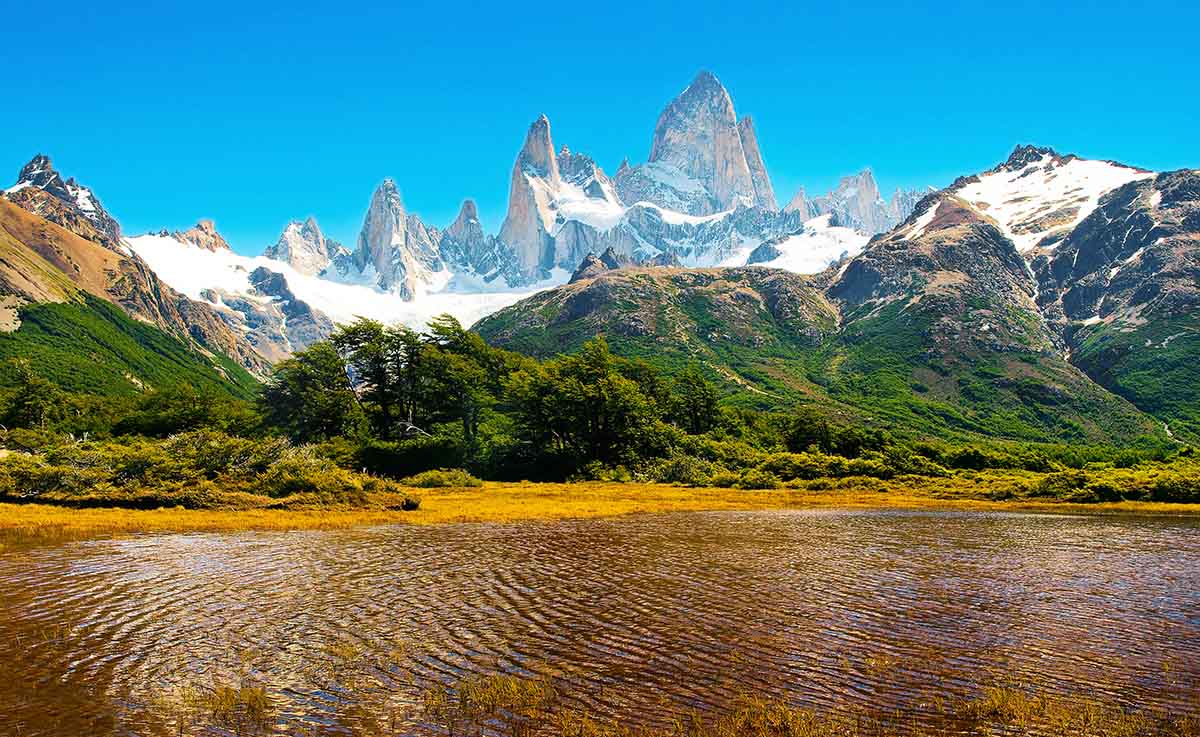 Granite peaks tower over green foothills behind the shallow edge of a lake.