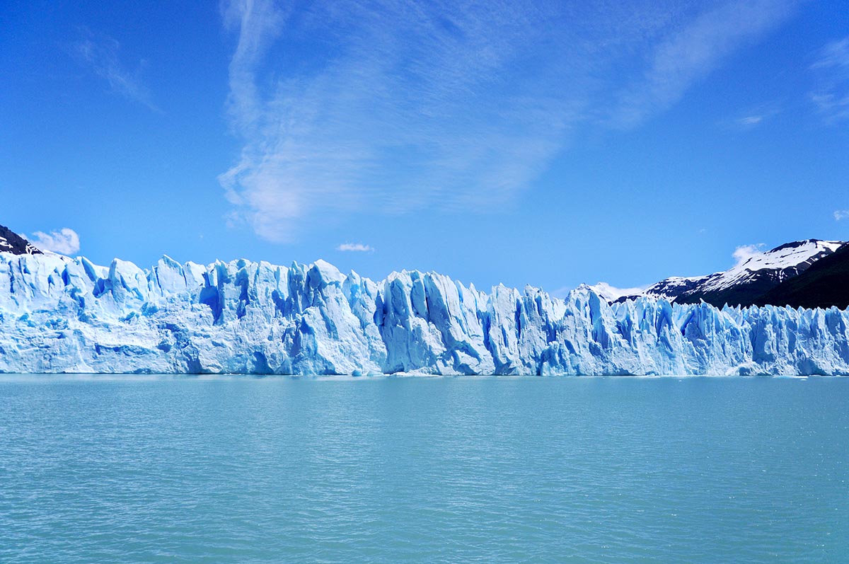 The outer edge of a light blue glacier stands over a blue lake.