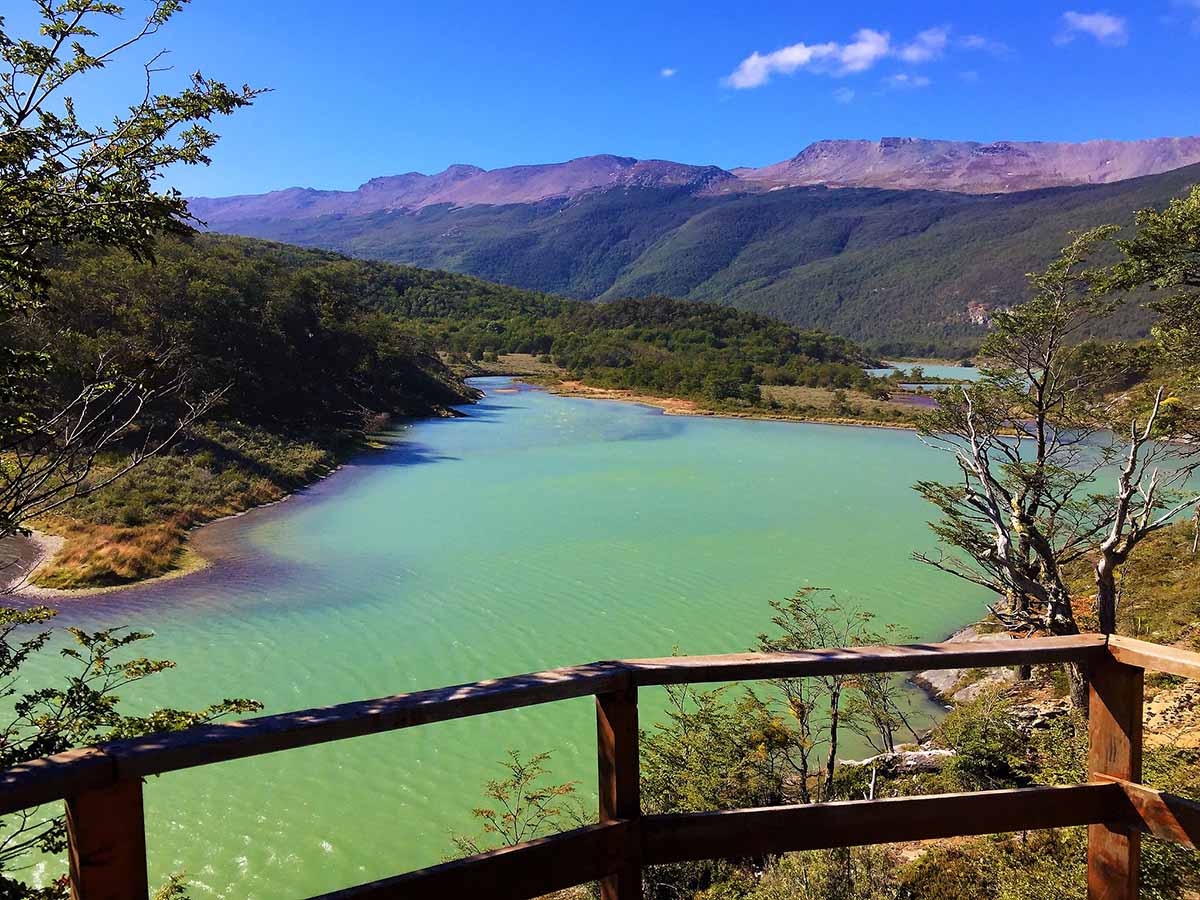 A railed lookout point over a turquoise lake surrounded by forested mountains.