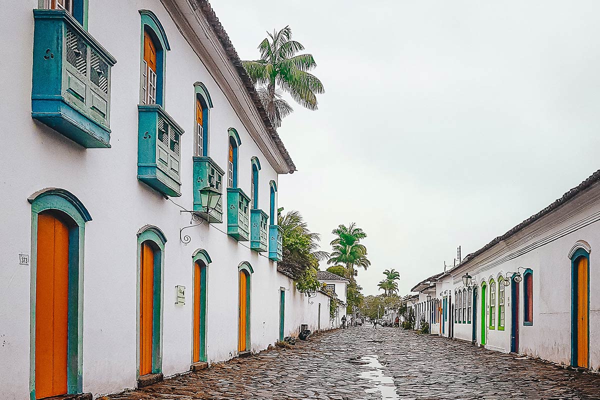 A wide stone street in downtown Paraty that's lines by white colonial-style buildings with colorful trim. 