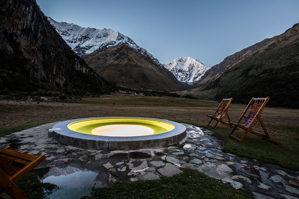 Two wooden chairs set up by an outside hot tub at night with snow-covered mountains. 