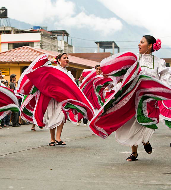 Women wearing red, white and green dresses and performing a traditional dance in Baños.