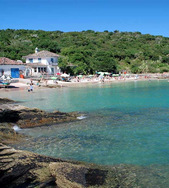 Visitors on a beach in Buzios with crystal blue water and surrounded by lush vegetation.