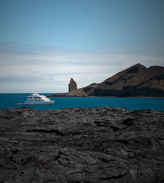 A yacht sails around dried lava flows and volcanic rock formations in the Galapagos Islands.