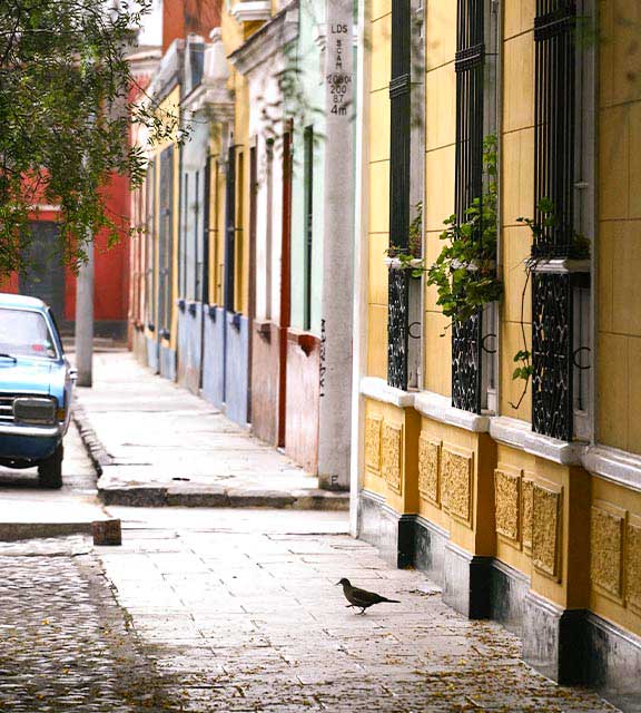 A car parked on a cobblestone street lined with colorful painted houses in Lima.