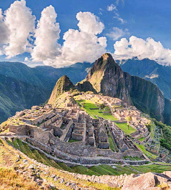 The ruins of Machu Picchu and surrounding mountains with a partially cloudy sky overhead.