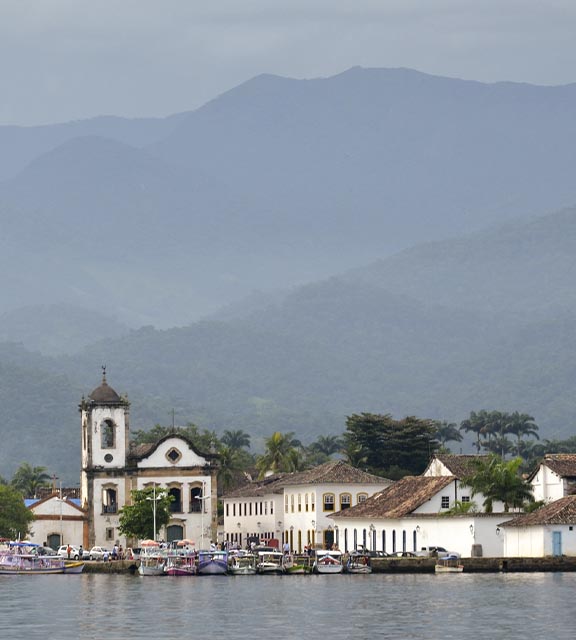 Boats in the water near the St. Rita church in Paraty, with forest-covered hills surrounding.