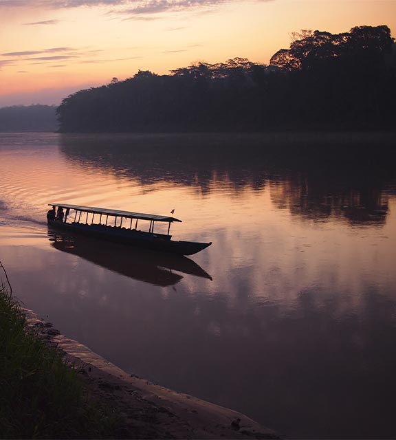 The sun setting and a boat navigating a river in the Amazon Rainforest near Puerto Maldonado.