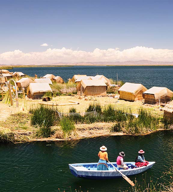 Three local people in a row boat next to one of the man-made Uros Islands in Lake Titicaca.