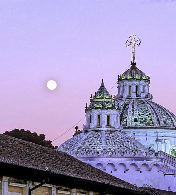 A pink and purple sky over the domed rooftops of the Compania de Jesus Church in Quito.