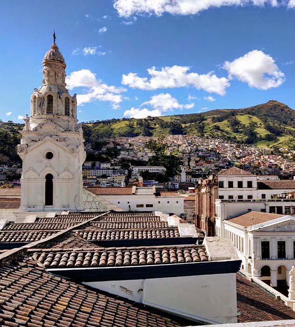 The Metropolitan Cathedral of Quito surrounded by green hillsides lined with houses.