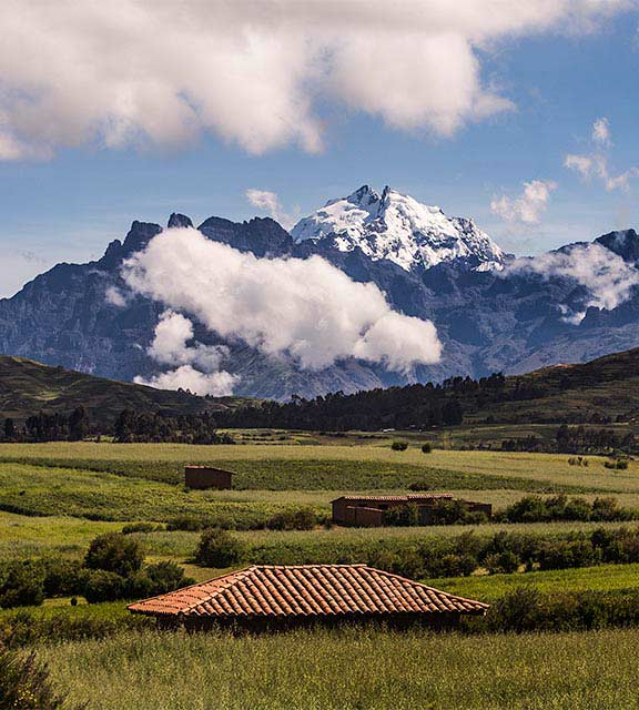 Snow-capped Andean mountains overlooking a green area dotted with rooftops in the Sacred Valley.
