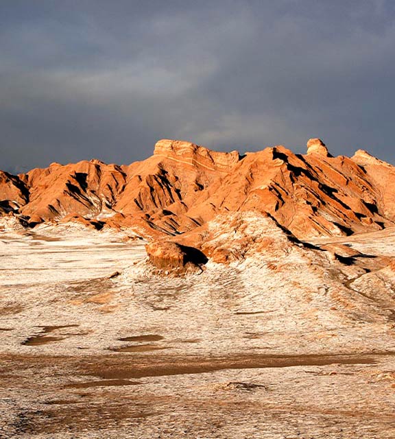 Jagged red rock formations covered in frost underneath a dark sky in the Atacama Desert.
