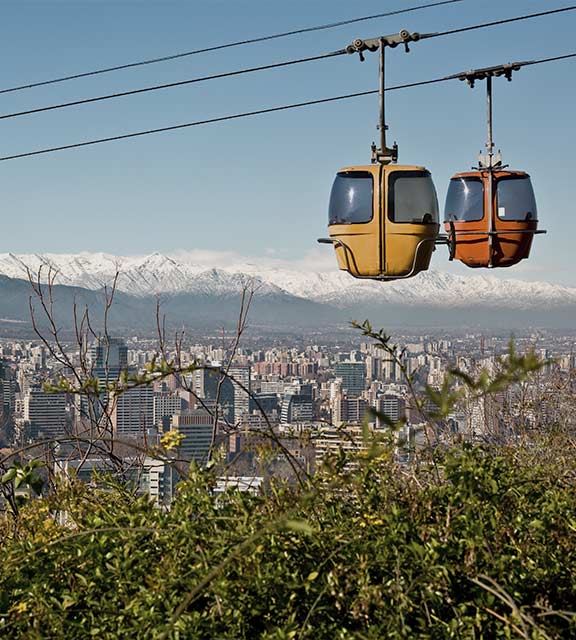 A pair of cable cars overlooking the city of Santiago with the Andes Mountains as a backdrop.