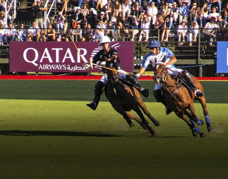 Crowds of people look on as two men on horseback play polo at a match in Argentina.