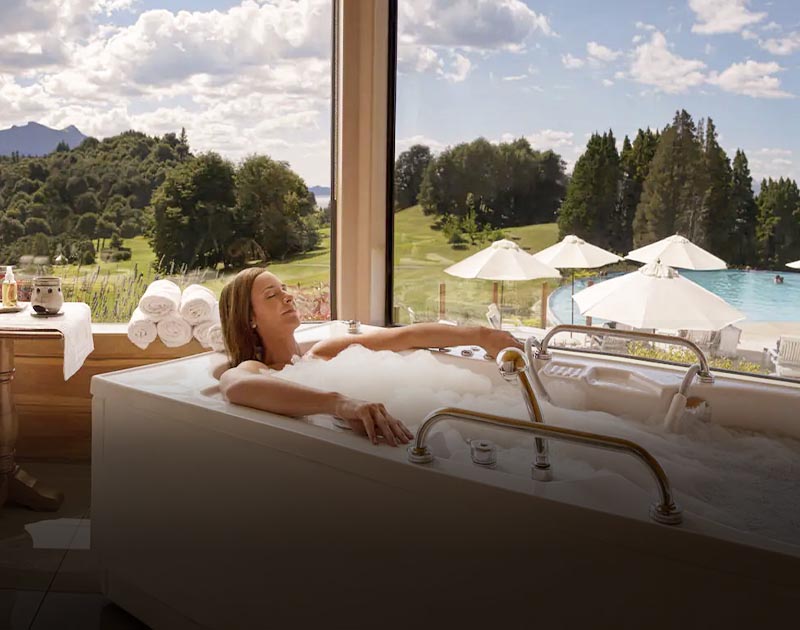 A woman in a bubble bath with windows facing an outdoor pool at Hotel Llao Llao in Bariloche.